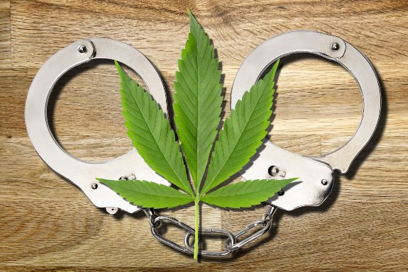 A marijuana leaf laying on a set of police handcuffs, symbolizing Record Eraser expunging your marijuana charges from your criminal record.